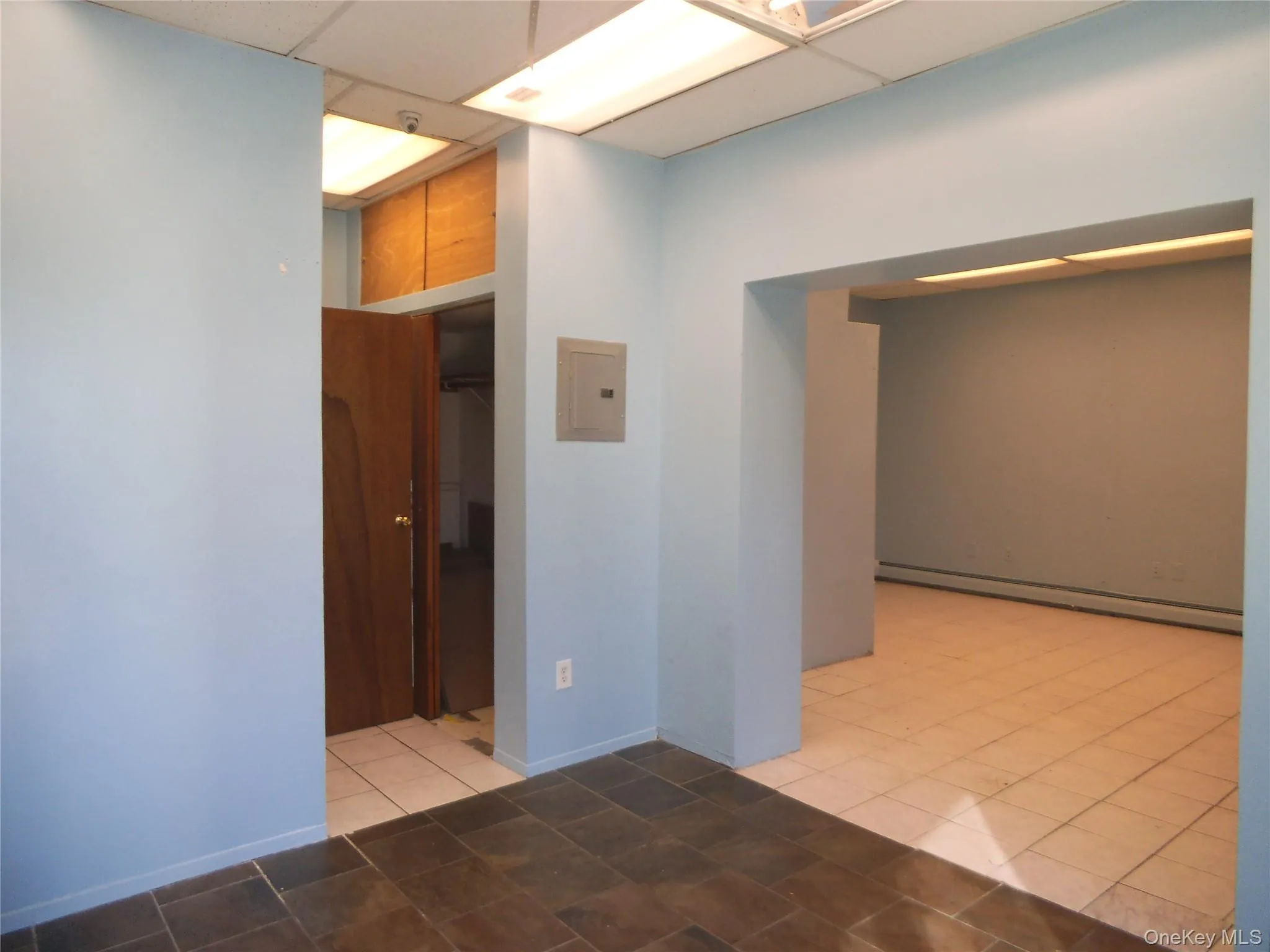 Unfurnished room with a drop ceiling, a baseboard radiator, electric panel, and light tile patterned floors Unfurnished room with a drop ceiling, a baseboard radiator, electric panel, and light tile patterned floors