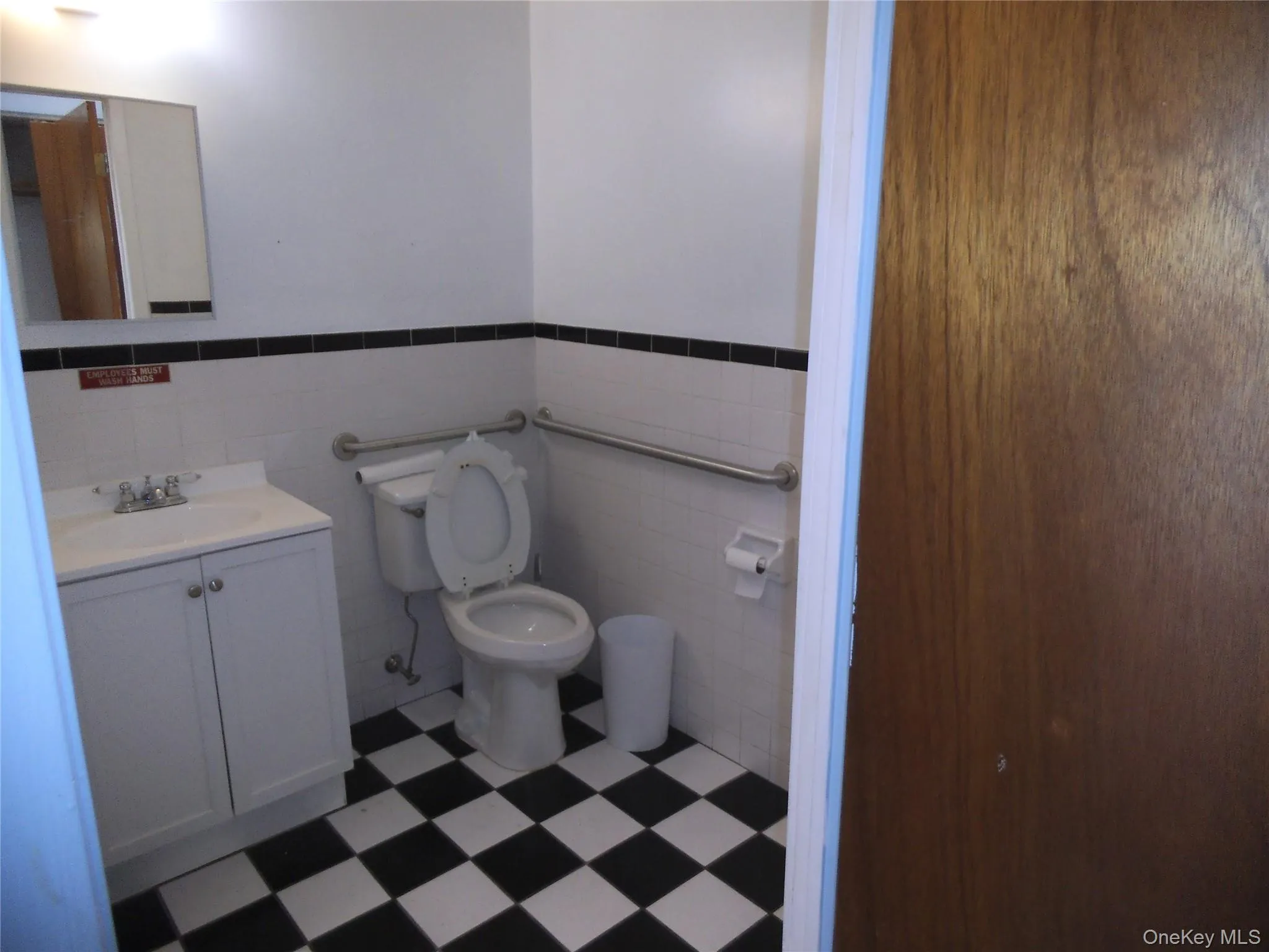 Half bathroom with vanity, tile walls, dark flooring, and a wainscoted wall Half bathroom with vanity, tile walls, dark flooring, and a wainscoted wall