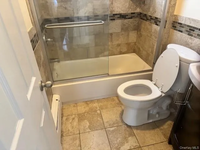 Bathroom with bath / shower combo with glass door, tile walls, vanity, baseboard heating, and light tile patterned floors Bathroom with bath / shower combo with glass door, tile walls, vanity, baseboard heating, and light tile patterned floors