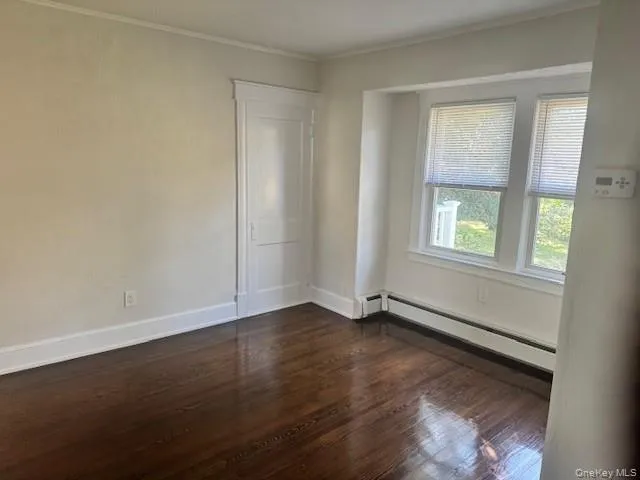 Empty room with dark wood-style floors, ornamental molding, and a baseboard heating unit Empty room with dark wood-style floors, ornamental molding, and a baseboard heating unit