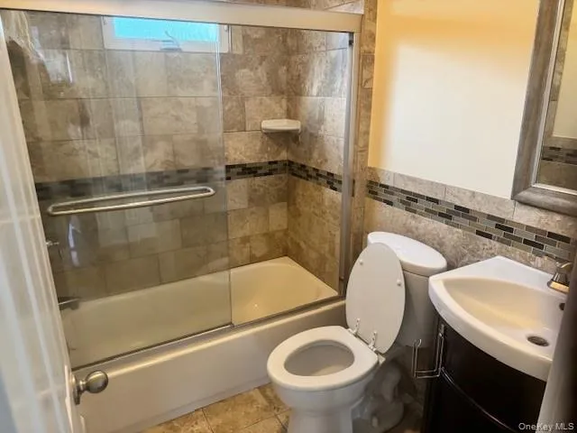 Full bathroom with vanity, shower / bath combination with glass door, tile walls, tile patterned floors, and a wainscoted wall Full bathroom with vanity, shower / bath combination with glass door, tile walls, tile patterned floors, and a wainscoted wall