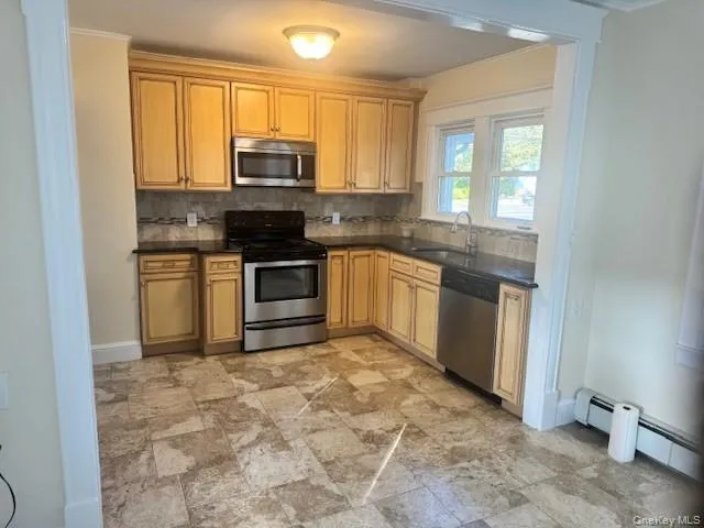 Kitchen with backsplash, appliances with stainless steel finishes, light stone finish floors, crown molding, and a baseboard heating unit Kitchen with backsplash, appliances with stainless steel finishes, light stone finish floors, crown molding, and a baseboard heating unit