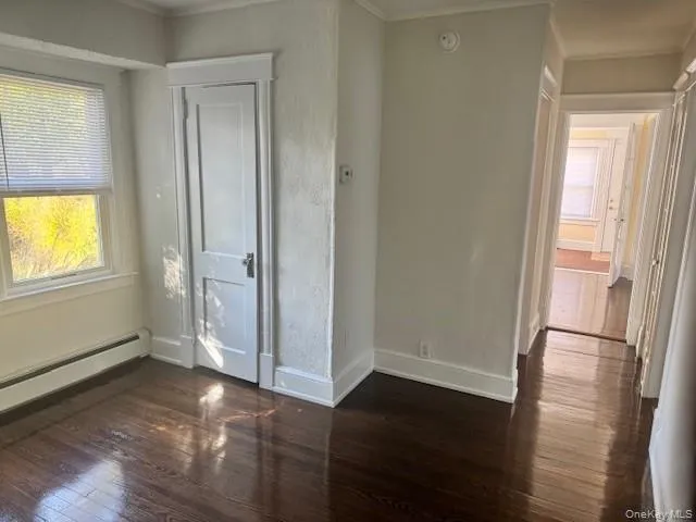 Unfurnished bedroom featuring dark wood-style floors and ornamental molding Unfurnished bedroom featuring dark wood-style floors and ornamental molding