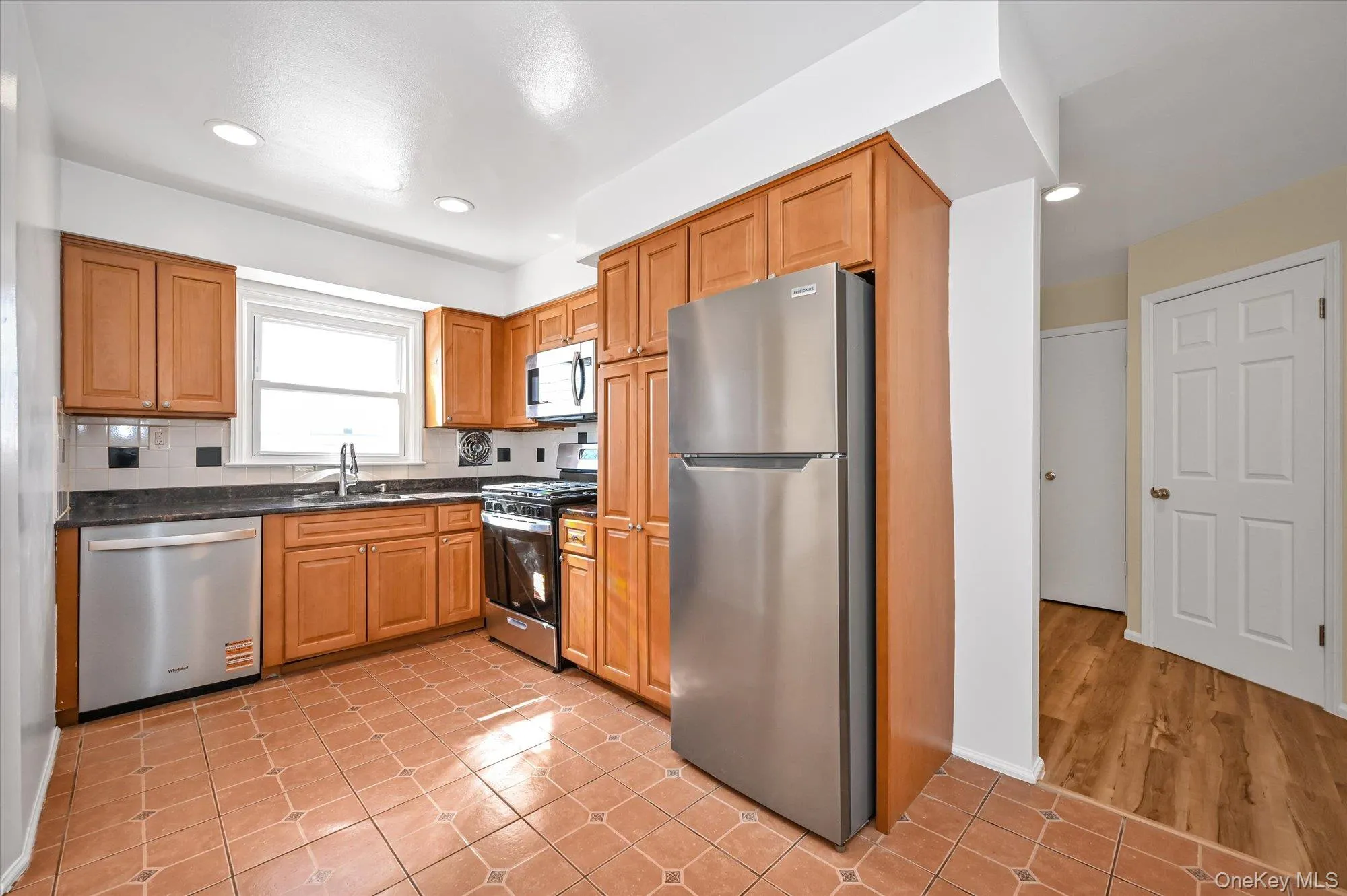 Kitchen with appliances with stainless steel finishes, light tile patterned floors, dark stone counters, recessed lighting, and brown cabinets Kitchen with appliances with stainless steel finishes, light tile patterned floors, dark stone counters, recessed lighting, and brown cabinets