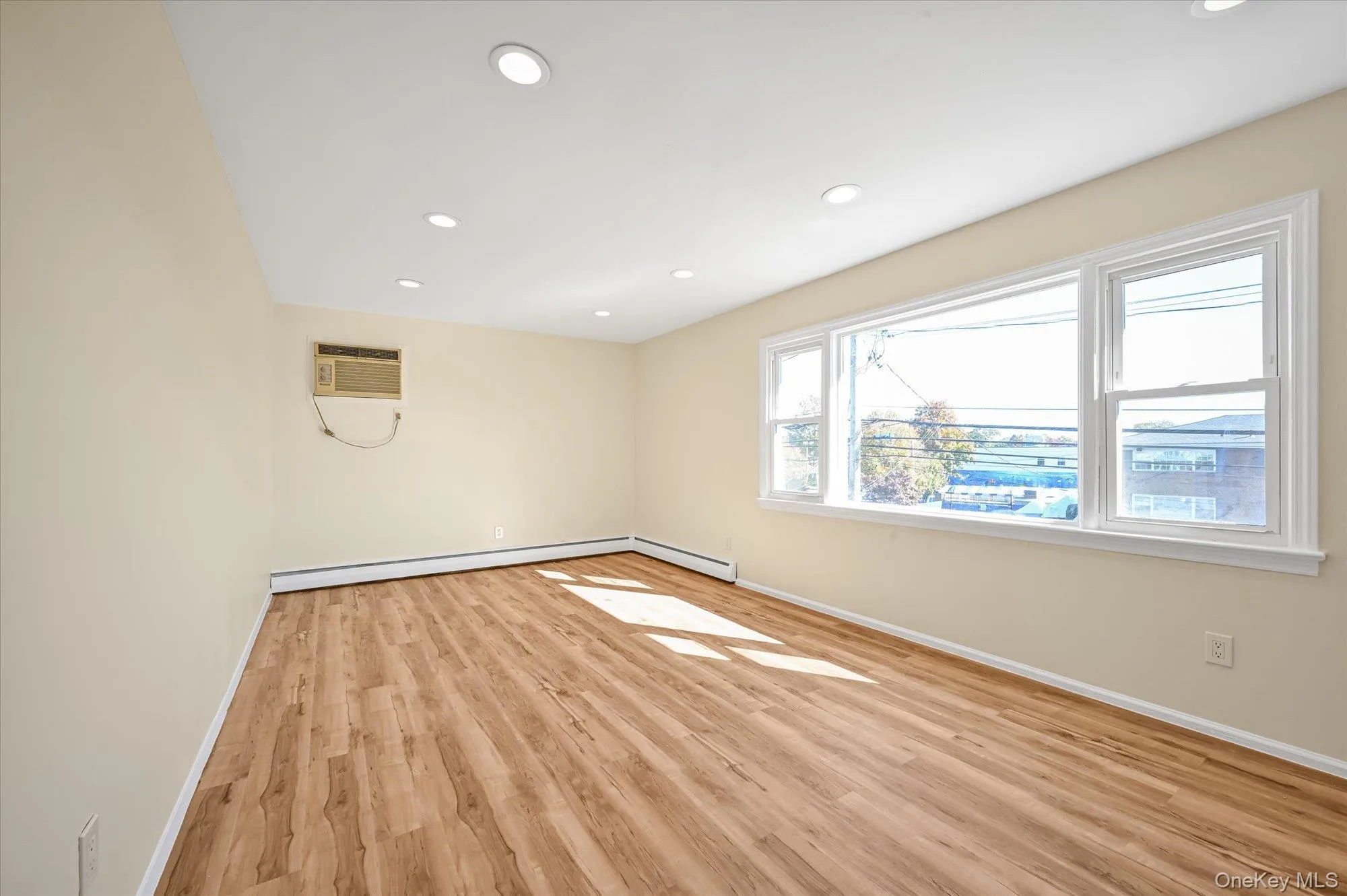 Empty room featuring recessed lighting, light wood-style floors, a wall mounted air conditioner, and baseboard heating Empty room featuring recessed lighting, light wood-style floors, a wall mounted air conditioner, and baseboard heating