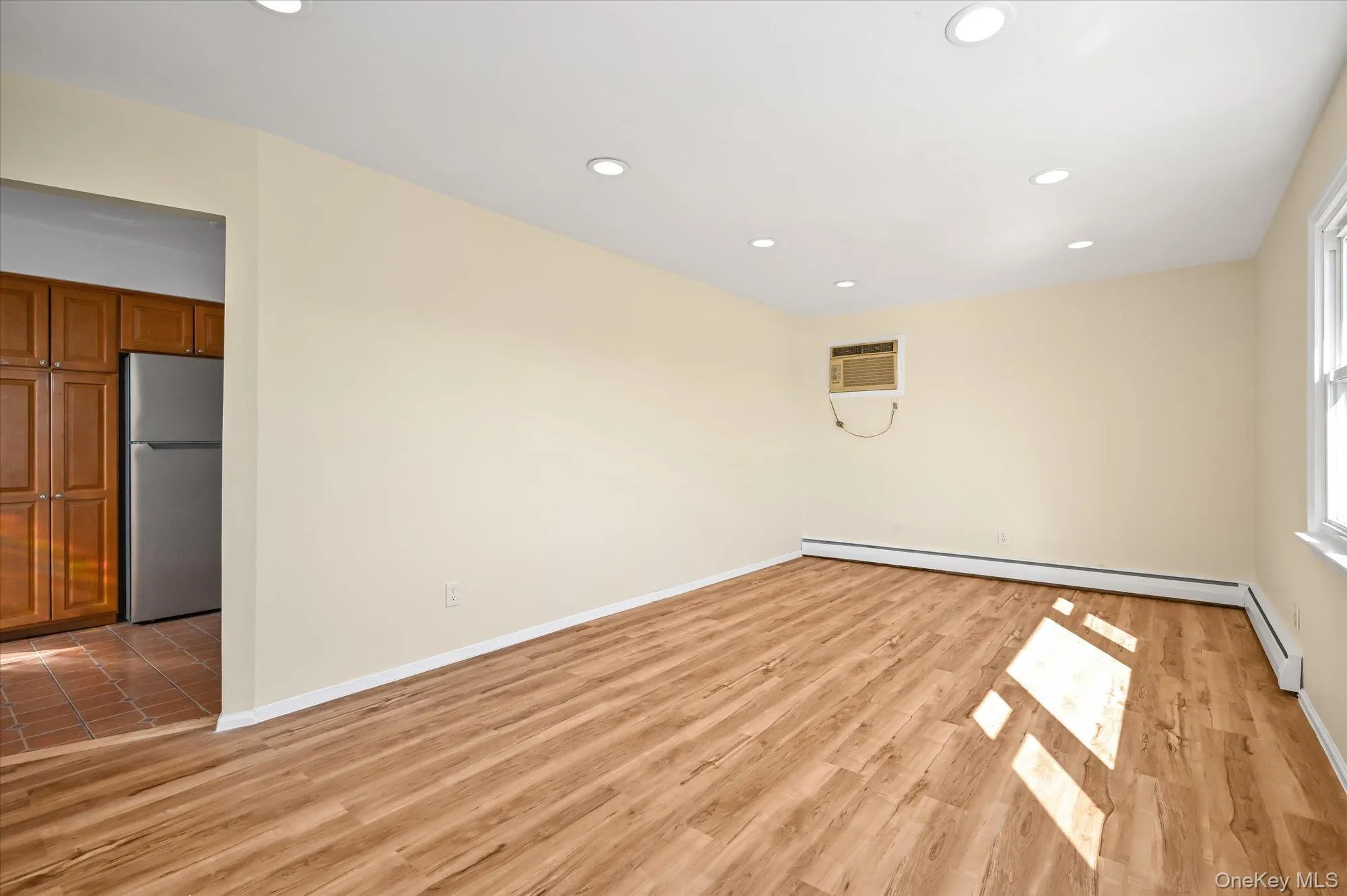 Empty room featuring recessed lighting, light wood-type flooring, a baseboard radiator, and a wall unit AC Empty room featuring recessed lighting, light wood-type flooring, a baseboard radiator, and a wall unit AC