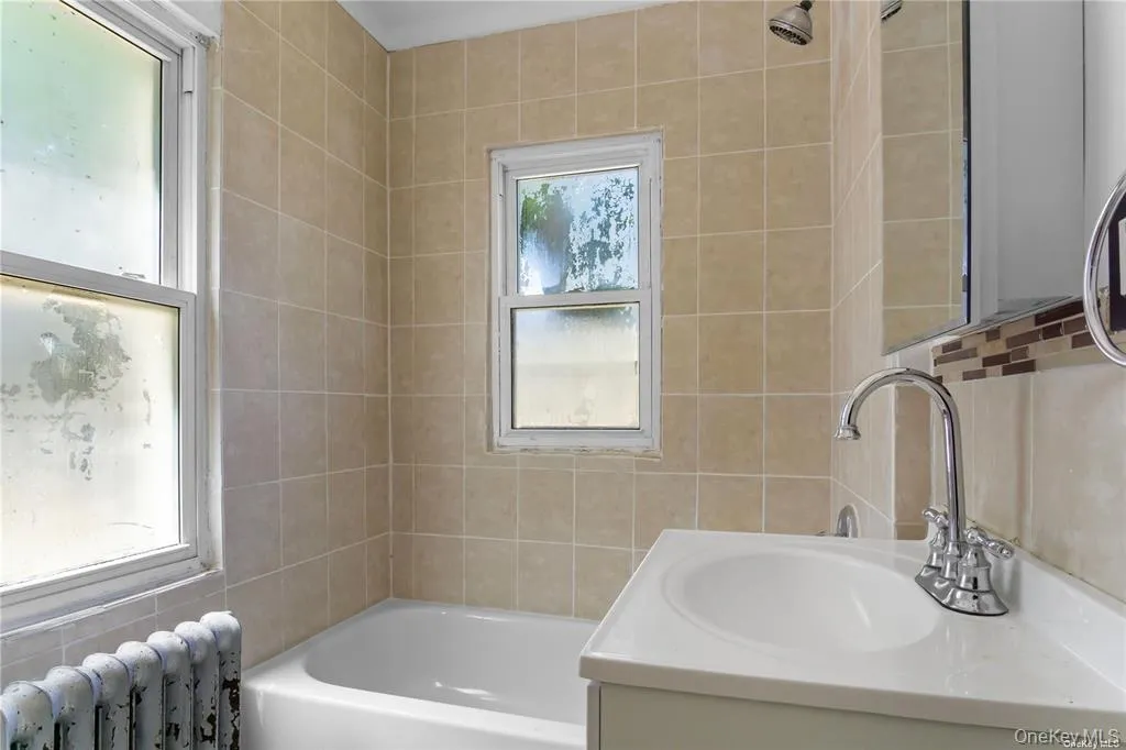 Bathroom with tile walls, radiator heating unit, a bathtub, plenty of natural light, and vanity Bathroom with tile walls, radiator heating unit, a bathtub, plenty of natural light, and vanity