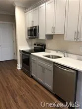 Kitchen with appliances with stainless steel finishes, light countertops, dark wood-type flooring, and gray cabinets Kitchen with appliances with stainless steel finishes, light countertops, dark wood-type flooring, and gray cabinets