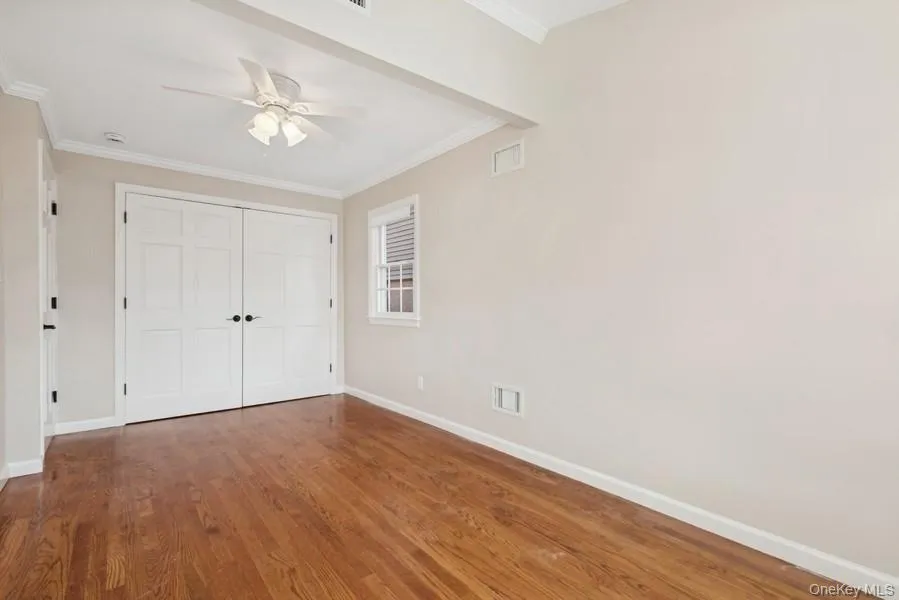 Unfurnished bedroom with ornamental molding, wood finished floors, a closet, and a ceiling fan Unfurnished bedroom with ornamental molding, wood finished floors, a closet, and a ceiling fan