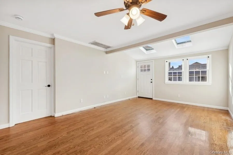 Unfurnished room featuring crown molding, light wood-style floors, a ceiling fan, and a skylight Unfurnished room featuring crown molding, light wood-style floors, a ceiling fan, and a skylight