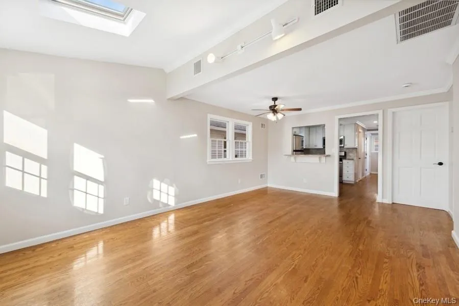 Unfurnished living room with light wood-style floors, ornamental molding, a skylight, a ceiling fan, and beam ceiling Unfurnished living room with light wood-style floors, ornamental molding, a skylight, a ceiling fan, and beam ceiling