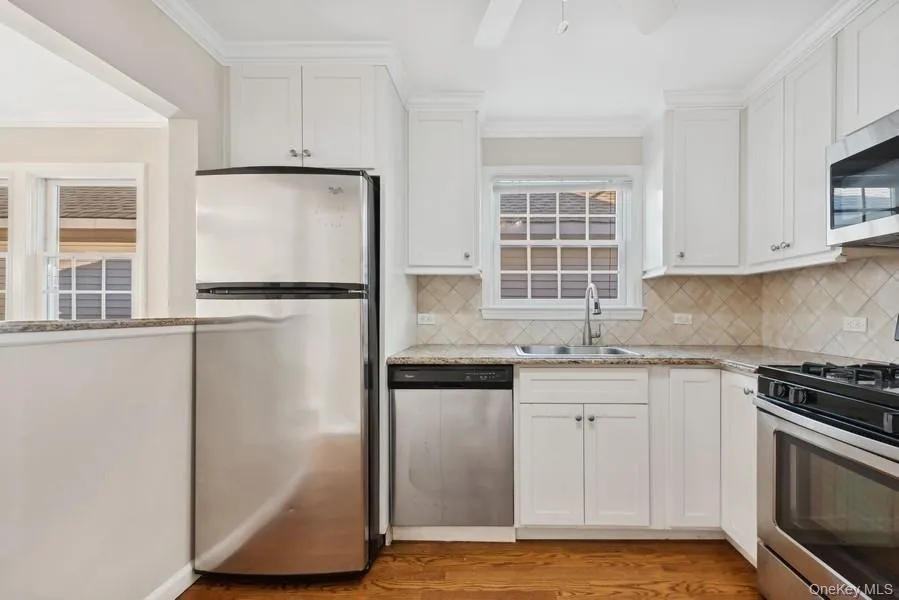 Kitchen featuring stainless steel appliances, crown molding, white cabinets, light stone counters, and light wood finished floors Kitchen featuring stainless steel appliances, crown molding, white cabinets, light stone counters, and light wood finished floors
