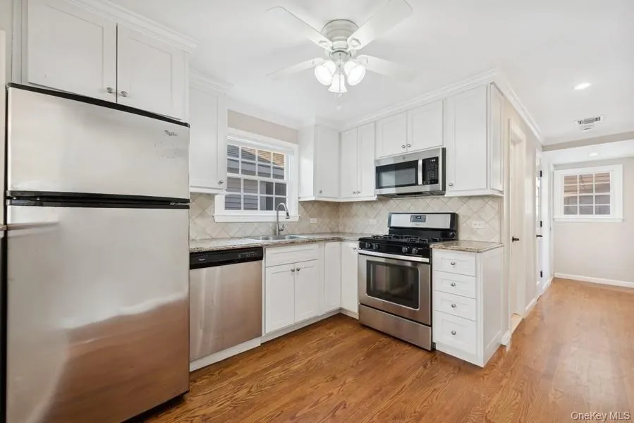 Kitchen featuring stainless steel appliances, white cabinets, light stone countertops, dark wood-style flooring, and recessed lighting Kitchen featuring stainless steel appliances, white cabinets, light stone countertops, dark wood-style flooring, and recessed lighting