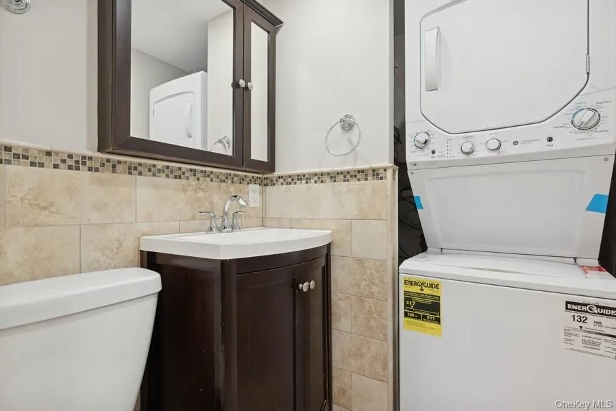 Bathroom with vanity, stacked washing machine and dryer, tile walls, and wainscoting Bathroom with vanity, stacked washing machine and dryer, tile walls, and wainscoting