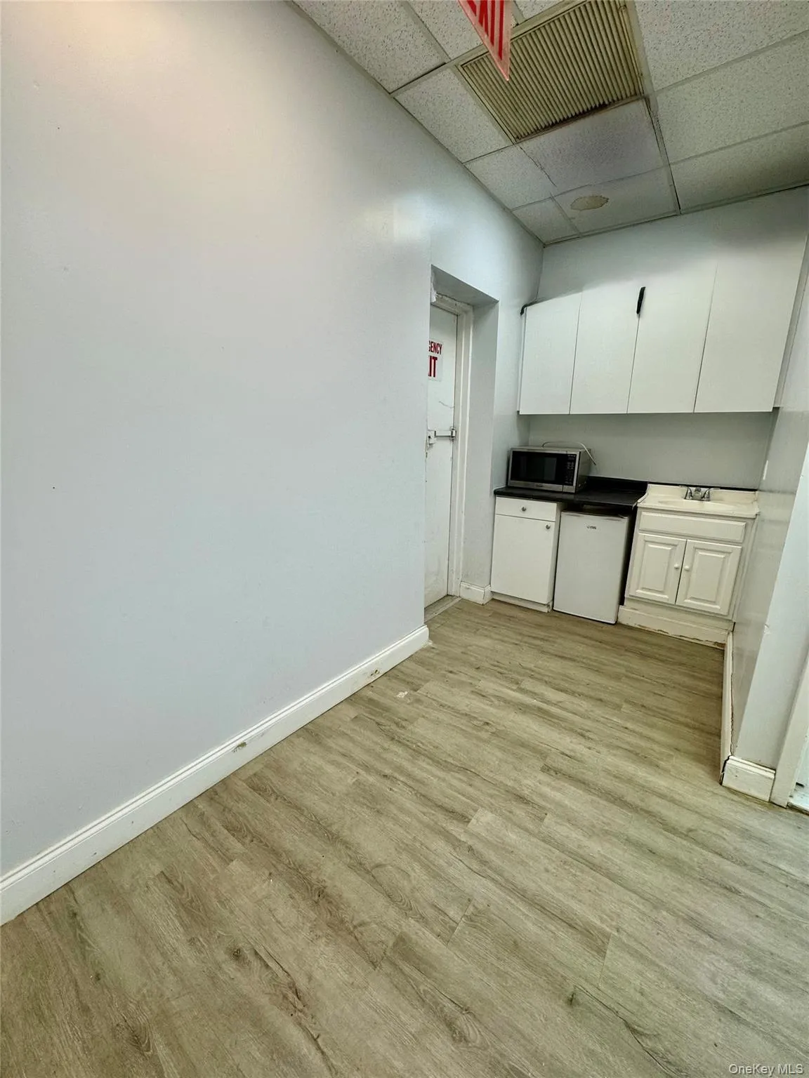 Kitchen featuring white cabinets, light wood-style flooring, a drop ceiling, dark countertops, and stainless steel microwave Kitchen featuring white cabinets, light wood-style flooring, a drop ceiling, dark countertops, and stainless steel microwave