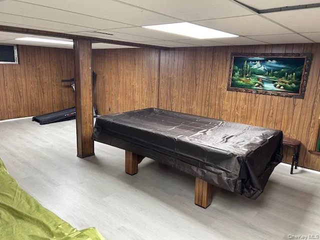 Game room featuring a paneled ceiling, wood walls, billiards table, and light wood-style flooring Game room featuring a paneled ceiling, wood walls, billiards table, and light wood-style flooring