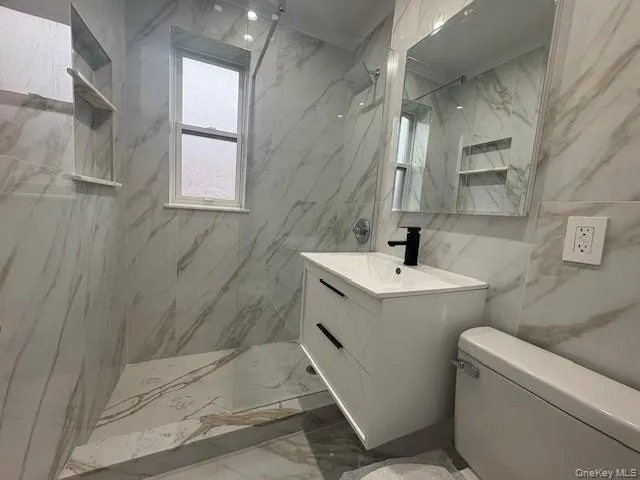 Full bath with marble style tiled floors, vanity, tile walls, a marble finish shower Full bath with marble style tiled floors, vanity, tile walls, a marble finish shower