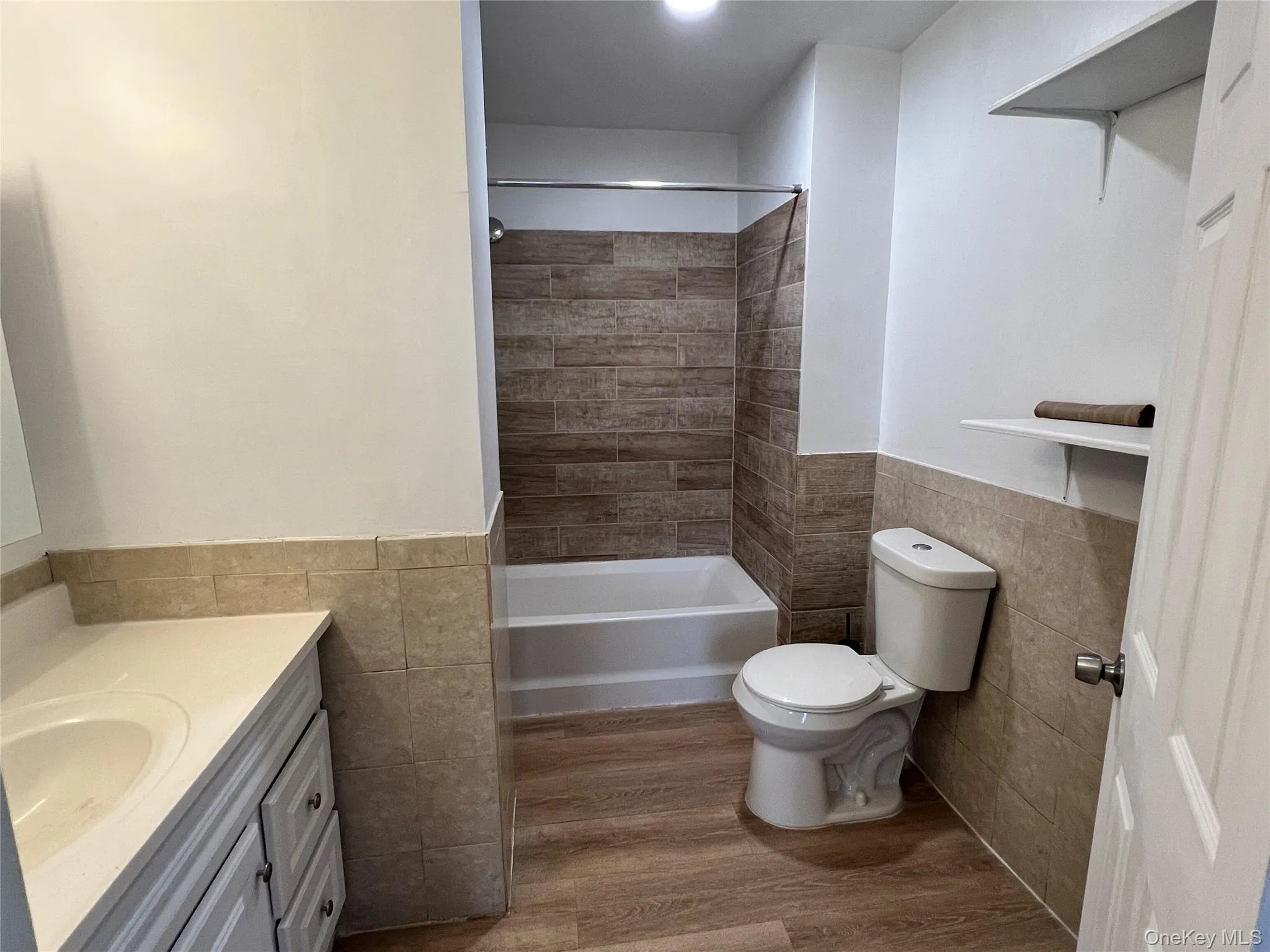 Full bath featuring tile walls, a wainscoted wall, light wood-type flooring, vanity, and shower / bathtub combination Full bath featuring tile walls, a wainscoted wall, light wood-type flooring, vanity, and shower / bathtub combination