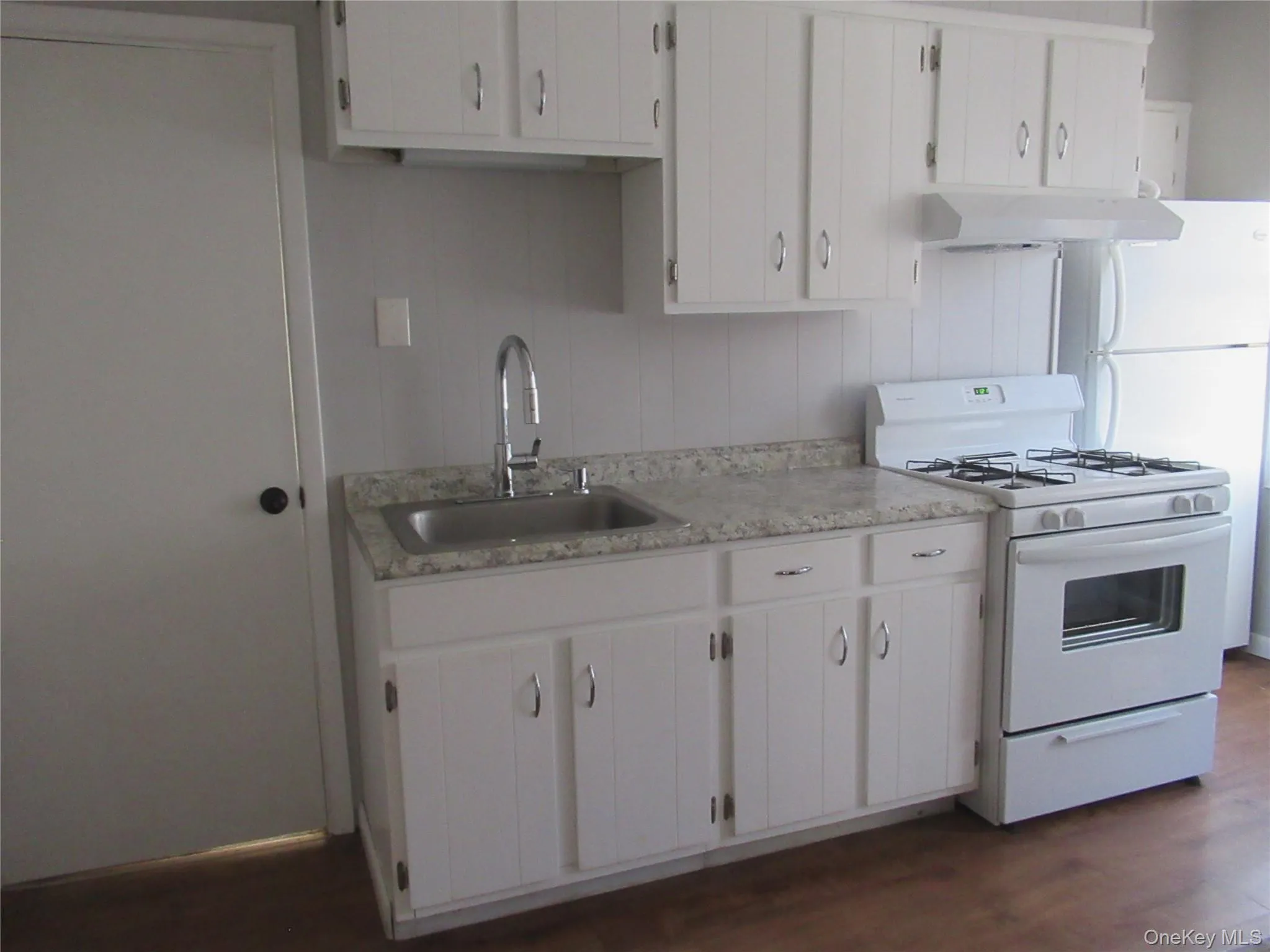 Kitchen featuring appliances, light countertops, white cabinets, wood-type flooring, and range hood back door down steps yard Kitchen featuring appliances, light countertops, white cabinets, wood-type flooring, and range hood back door down steps yard