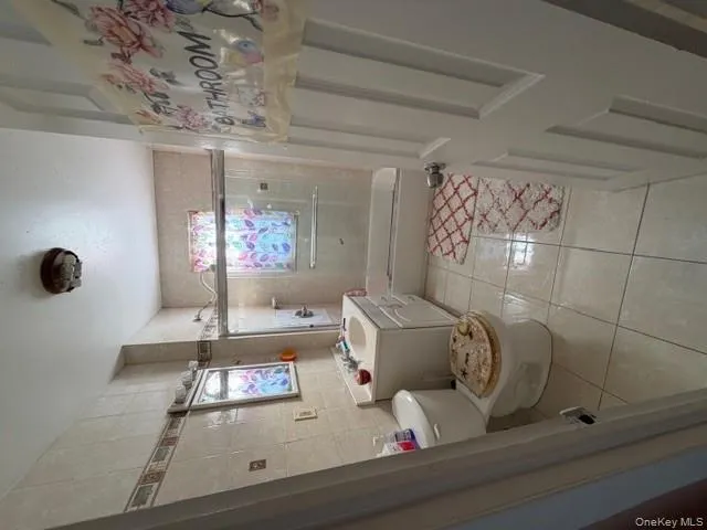 Full bath featuring light tile patterned floors, vanity, combined bath / shower with glass door, tile walls, and healthy amount of natural light Full bath featuring light tile patterned floors, vanity, combined bath / shower with glass door, tile walls, and healthy amount of natural light