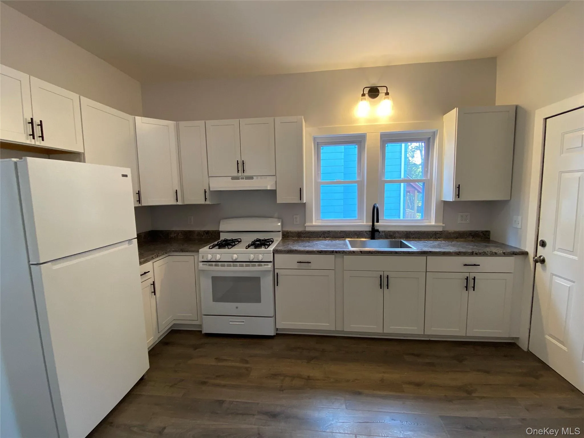 Kitchen with white appliances, white cabinetry, dark wood finished floors, and under cabinet range hood Kitchen with white appliances, white cabinetry, dark wood finished floors, and under cabinet range hood