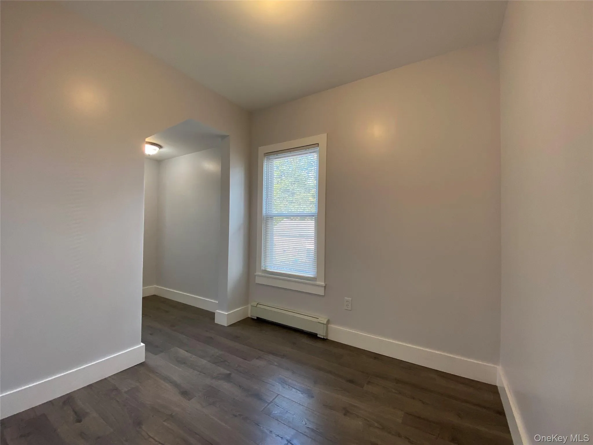 Unfurnished room featuring dark wood-style floors and baseboard heating Unfurnished room featuring dark wood-style floors and baseboard heating