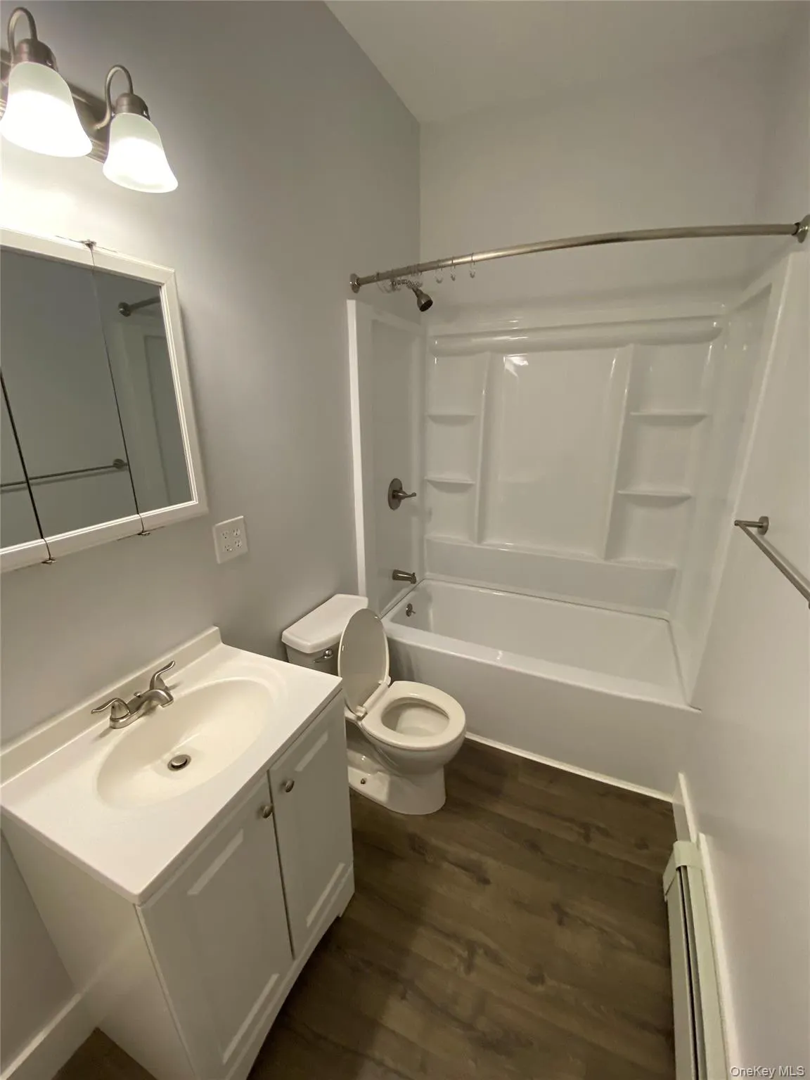 Bathroom featuring vanity, shower combination, dark wood-style floors, and a baseboard radiator Bathroom featuring vanity, shower combination, dark wood-style floors, and a baseboard radiator