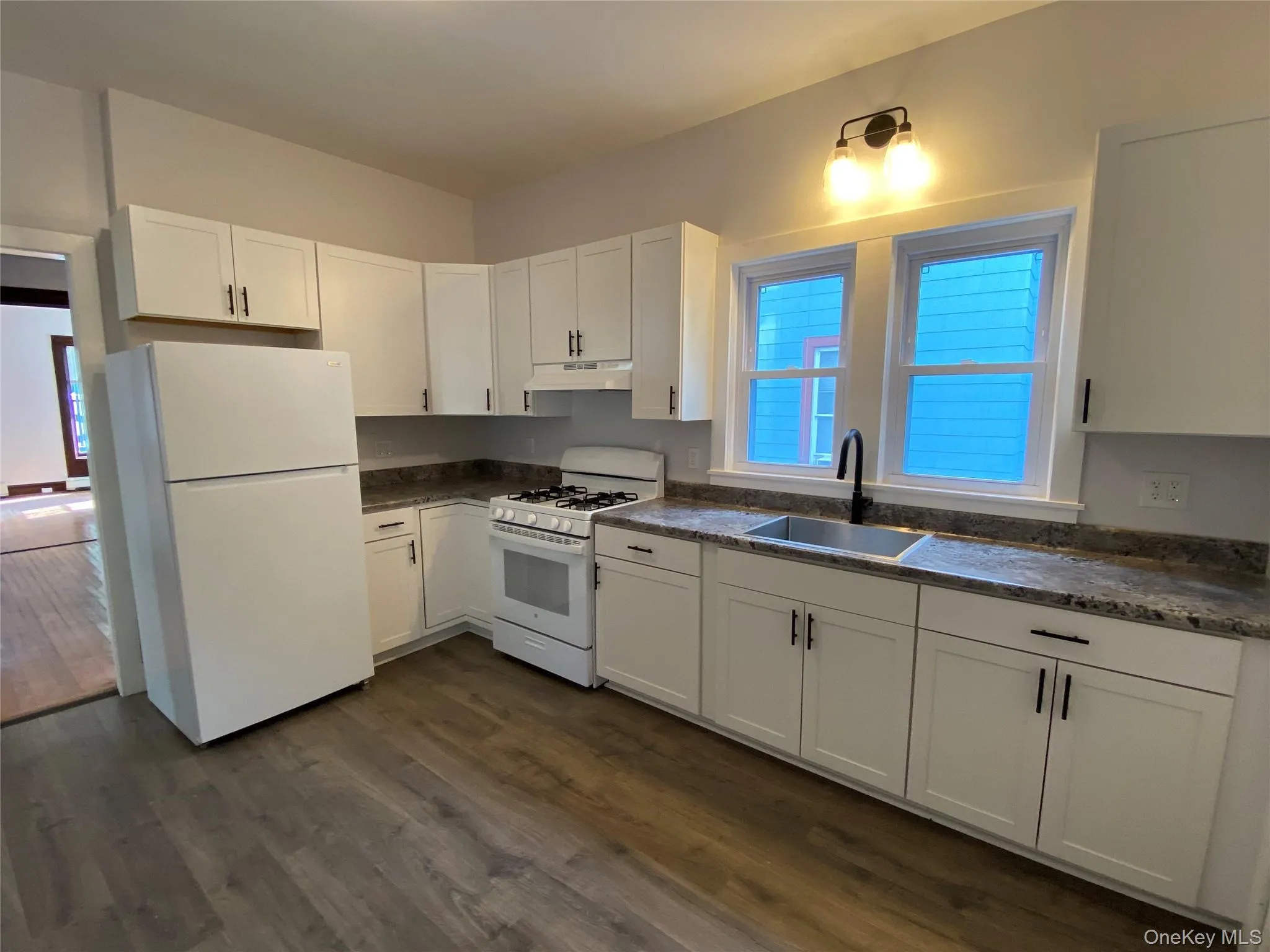 Kitchen featuring white cabinetry, white appliances, dark wood-style floors, and under cabinet range hood Kitchen featuring white cabinetry, white appliances, dark wood-style floors, and under cabinet range hood