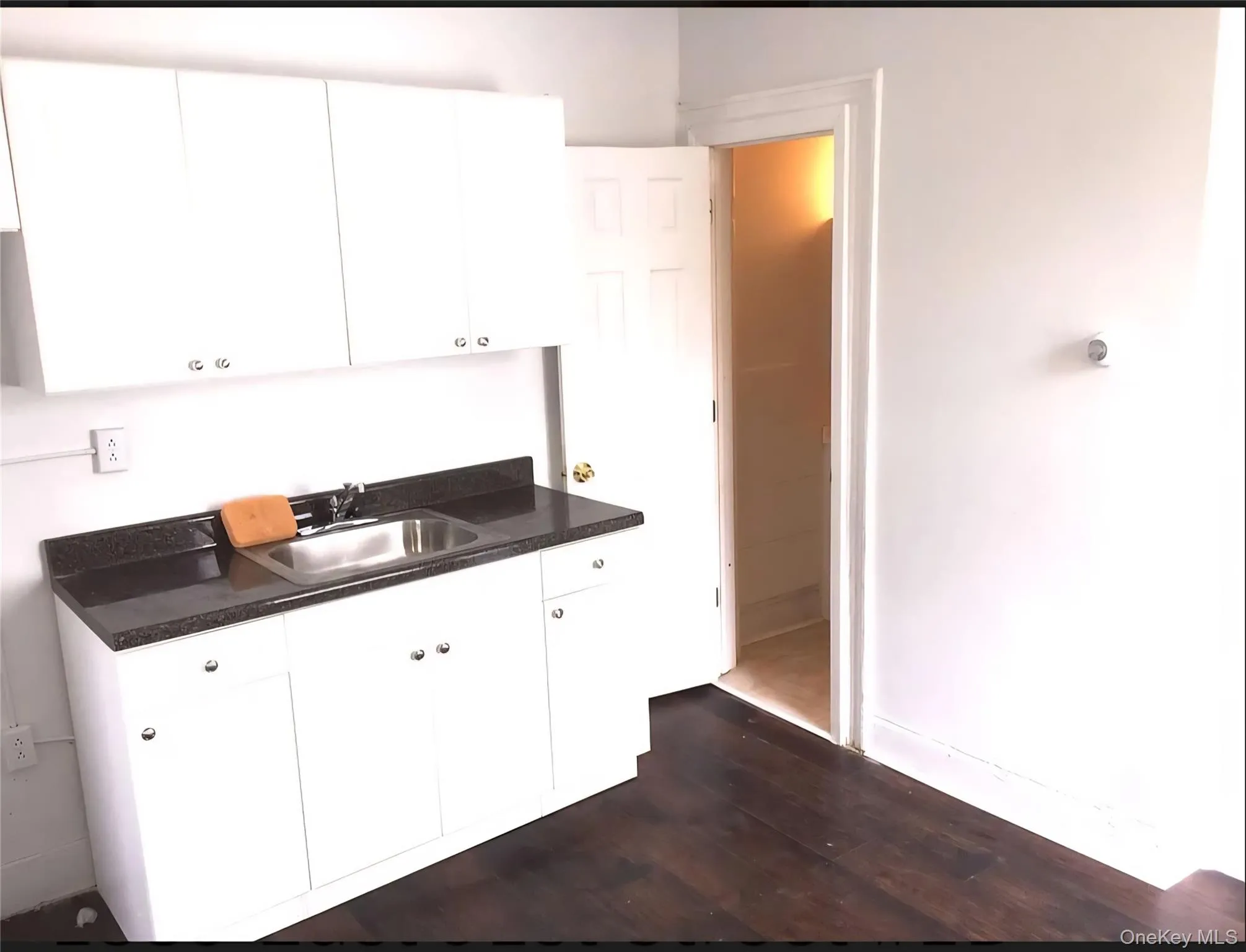 Kitchen with dark countertops, white cabinetry, and dark wood-style flooring Kitchen with dark countertops, white cabinetry, and dark wood-style flooring