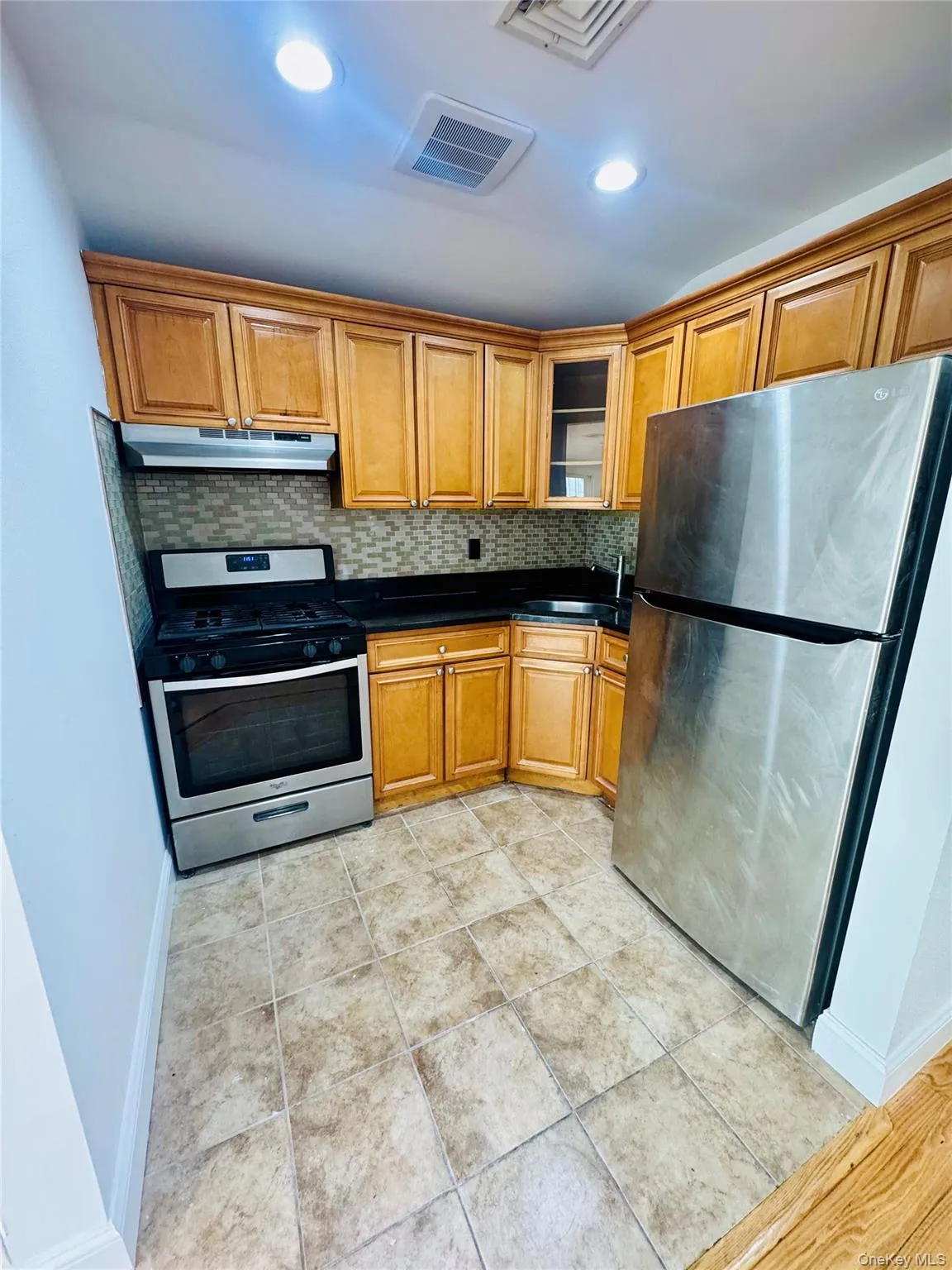 Kitchen featuring stainless steel appliances, dark countertops, brown cabinets, tasteful backsplash, and glass insert cabinets Kitchen featuring stainless steel appliances, dark countertops, brown cabinets, tasteful backsplash, and glass insert cabinets