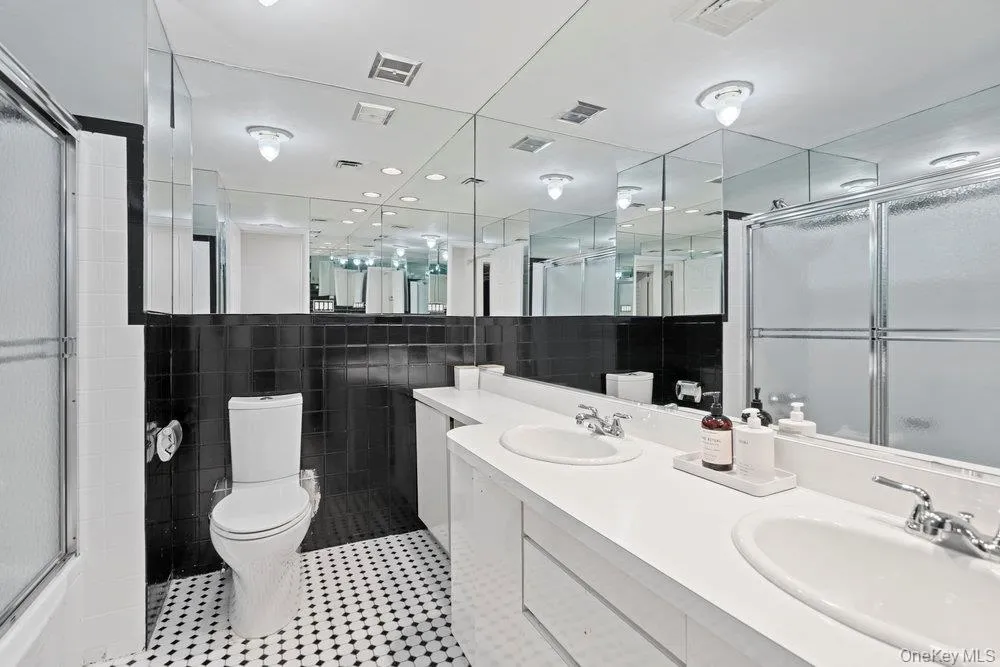 Full bathroom featuring double vanity, tile walls, and light tile patterned floors Full bathroom featuring double vanity, tile walls, and light tile patterned floors