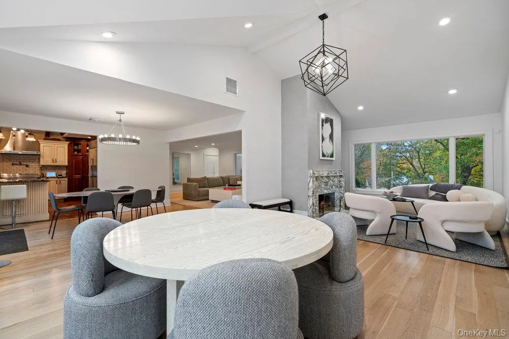 Dining room with a chandelier, recessed lighting, light wood-style flooring, a stone fireplace, and high vaulted ceiling Dining room with a chandelier, recessed lighting, light wood-style flooring, a stone fireplace, and high vaulted ceiling