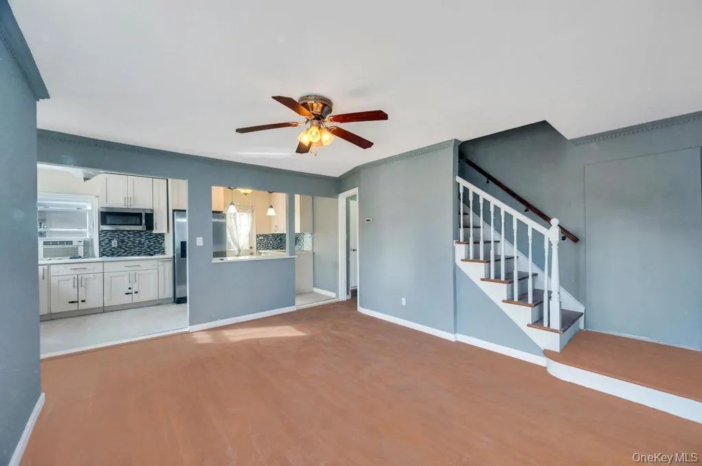 Unfurnished living room with light wood-style flooring, stairway, ceiling fan, and cooling unit Unfurnished living room with light wood-style flooring, stairway, ceiling fan, and cooling unit
