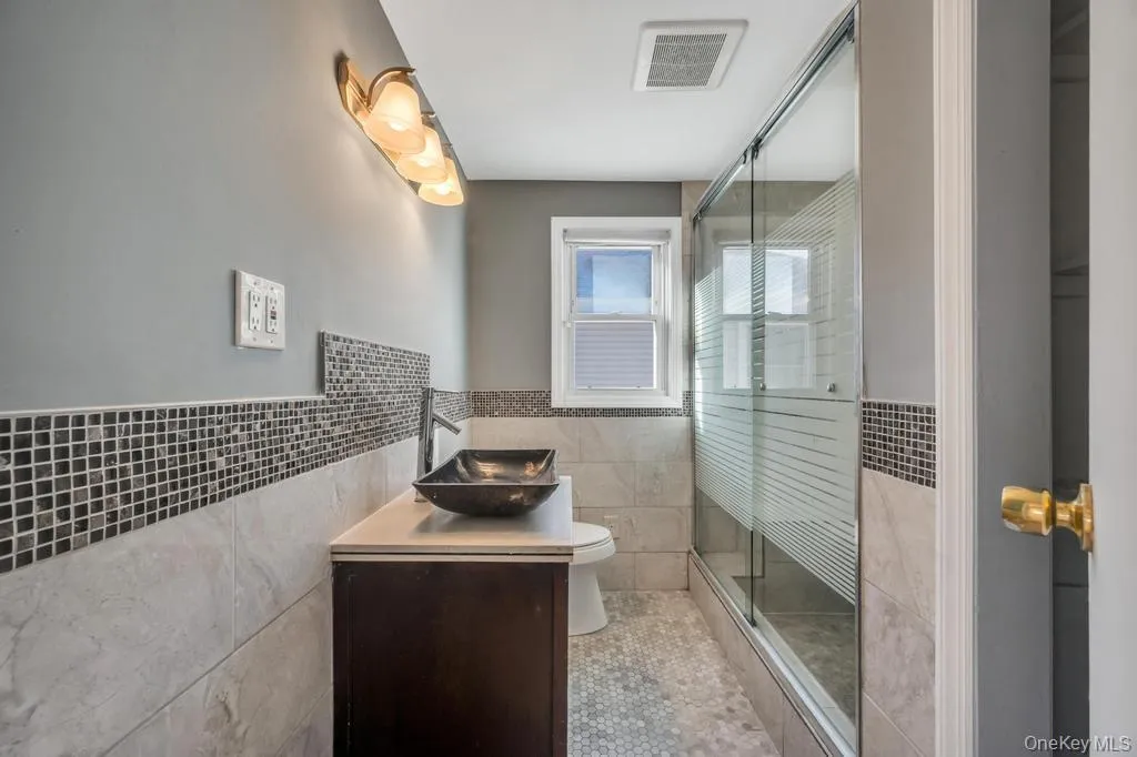 Bathroom featuring tile walls, a wainscoted wall, vanity, and a shower stall Bathroom featuring tile walls, a wainscoted wall, vanity, and a shower stall
