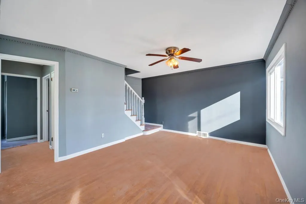 Unfurnished living room with wood finished floors, ceiling fan, ornamental molding, and stairway Unfurnished living room with wood finished floors, ceiling fan, ornamental molding, and stairway
