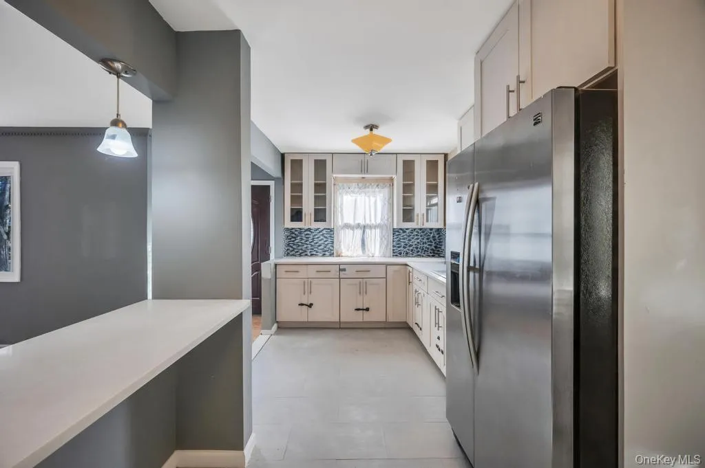 Kitchen with stainless steel fridge, decorative light fixtures, backsplash, glass insert cabinets, and light tile patterned floors Kitchen with stainless steel fridge, decorative light fixtures, backsplash, glass insert cabinets, and light tile patterned floors