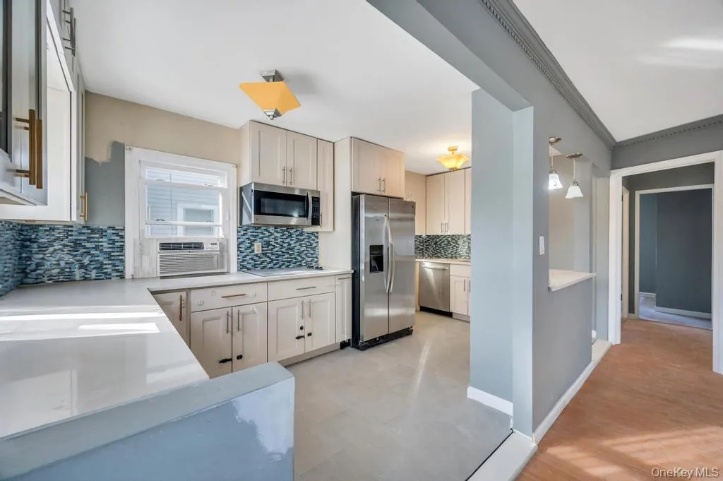 Kitchen featuring tasteful backsplash, appliances with stainless steel finishes, light stone countertops, ornamental molding, and cooling unit Kitchen featuring tasteful backsplash, appliances with stainless steel finishes, light stone countertops, ornamental molding, and cooling unit