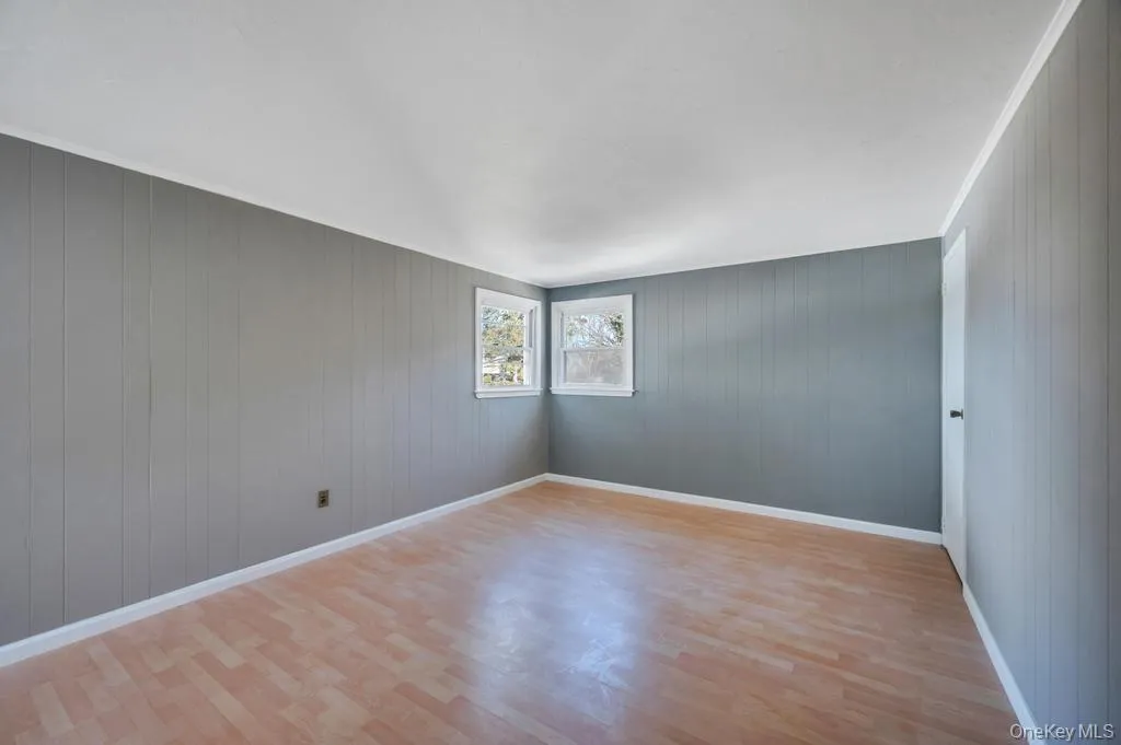 Empty room featuring wood walls, light wood-type flooring, and crown molding Empty room featuring wood walls, light wood-type flooring, and crown molding
