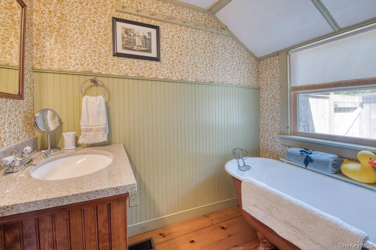 Full bath featuring a freestanding tub, vanity, wood finished floors, lofted ceiling, and wallpapered walls Full bath featuring a freestanding tub, vanity, wood finished floors, lofted ceiling, and wallpapered walls