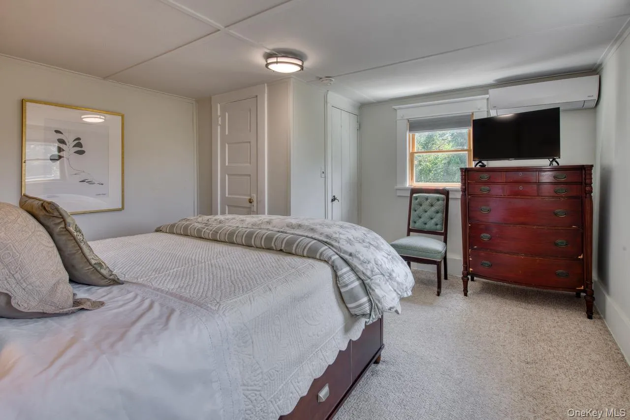 Bedroom with light colored carpet and an AC wall unit Bedroom with light colored carpet and an AC wall unit