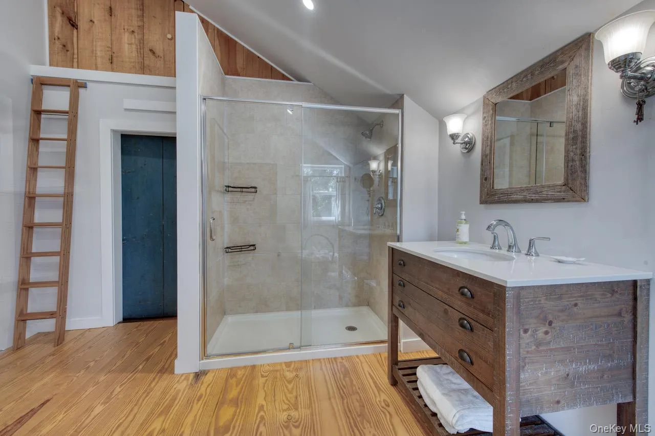 Full bathroom featuring light wood finished floors, vanity, a stall shower, and vaulted ceiling Full bathroom featuring light wood finished floors, vanity, a stall shower, and vaulted ceiling