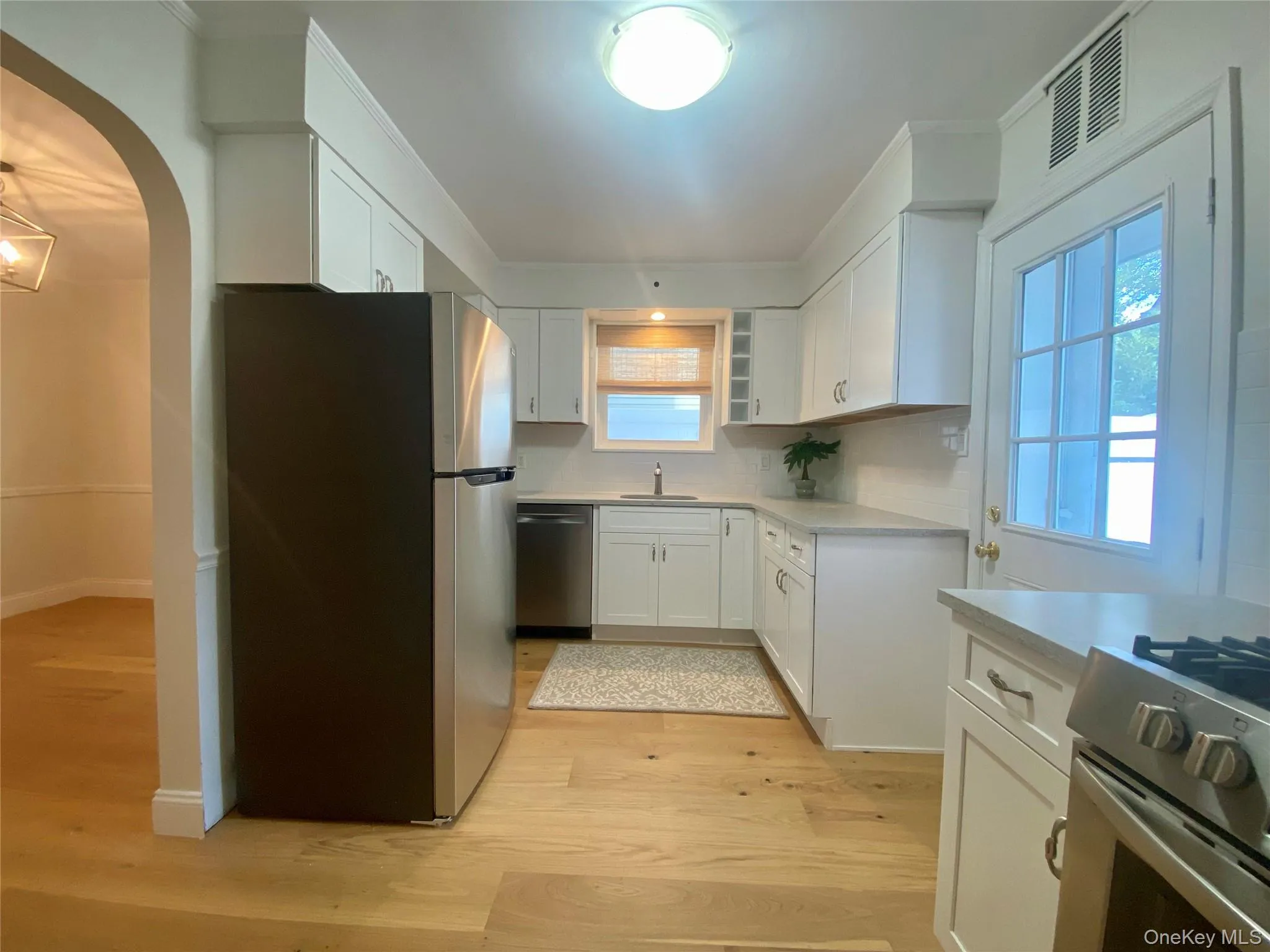 Kitchen featuring white cabinets, stainless steel appliances, arched walkways, and light wood finished floors Kitchen featuring white cabinets, stainless steel appliances, arched walkways, and light wood finished floors