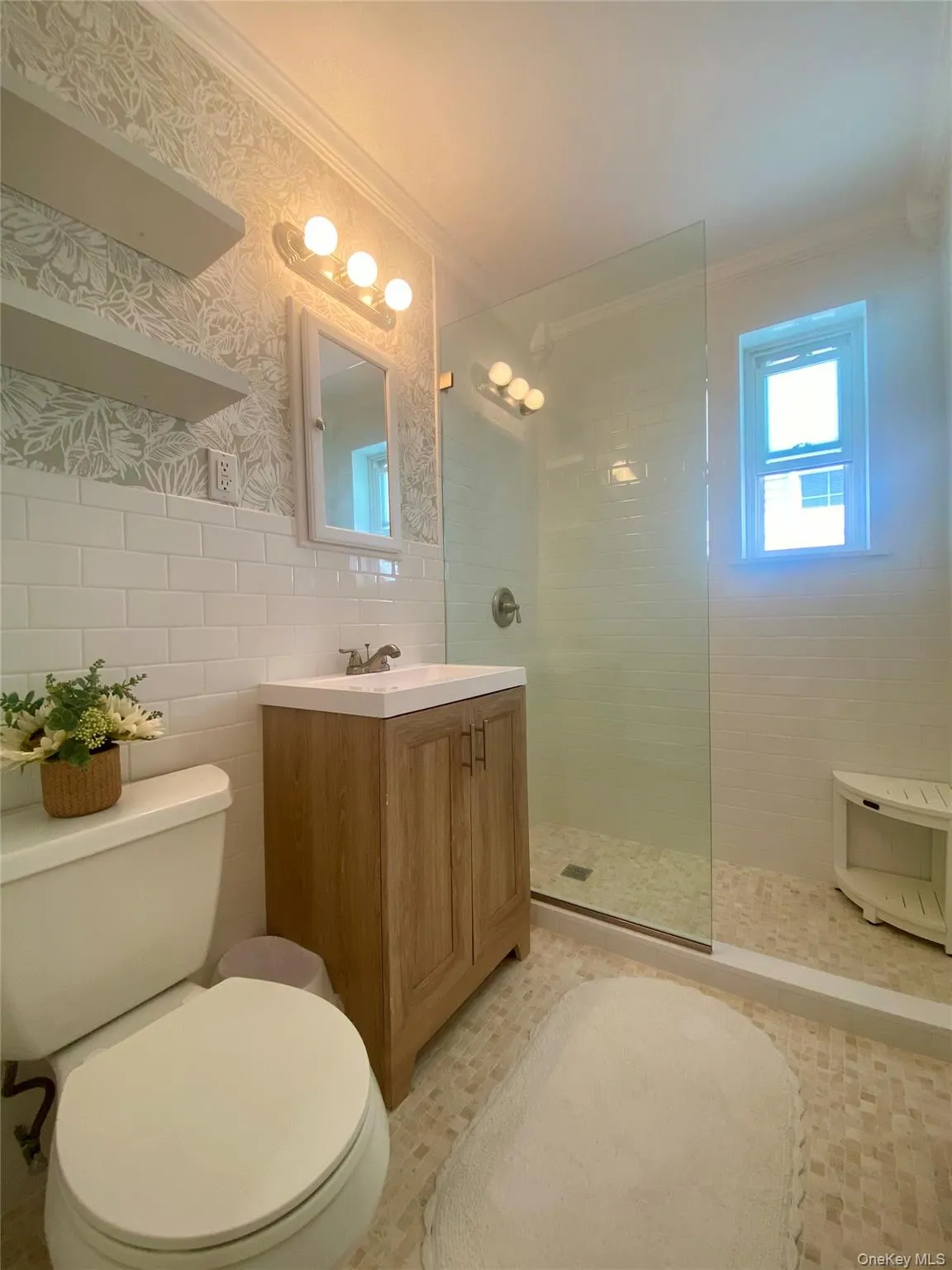 Full bathroom featuring tile walls, walk in shower, vanity, ornamental molding, and wallpapered walls Full bathroom featuring tile walls, walk in shower, vanity, ornamental molding, and wallpapered walls