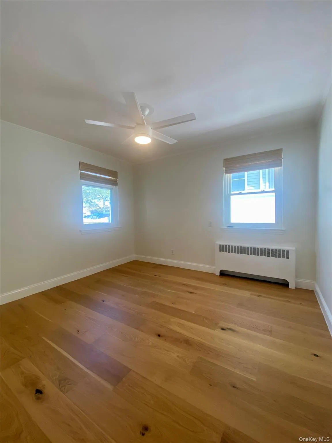 Spare room featuring radiator heating unit, light wood-style floors, crown molding, and a ceiling fan Spare room featuring radiator heating unit, light wood-style floors, crown molding, and a ceiling fan