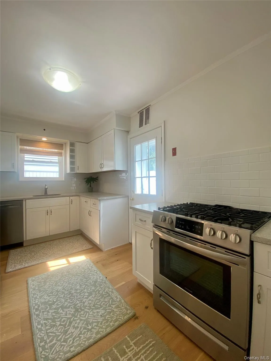 Kitchen with stainless steel appliances, white cabinets, tasteful backsplash, crown molding, and light wood-style floors Kitchen with stainless steel appliances, white cabinets, tasteful backsplash, crown molding, and light wood-style floors