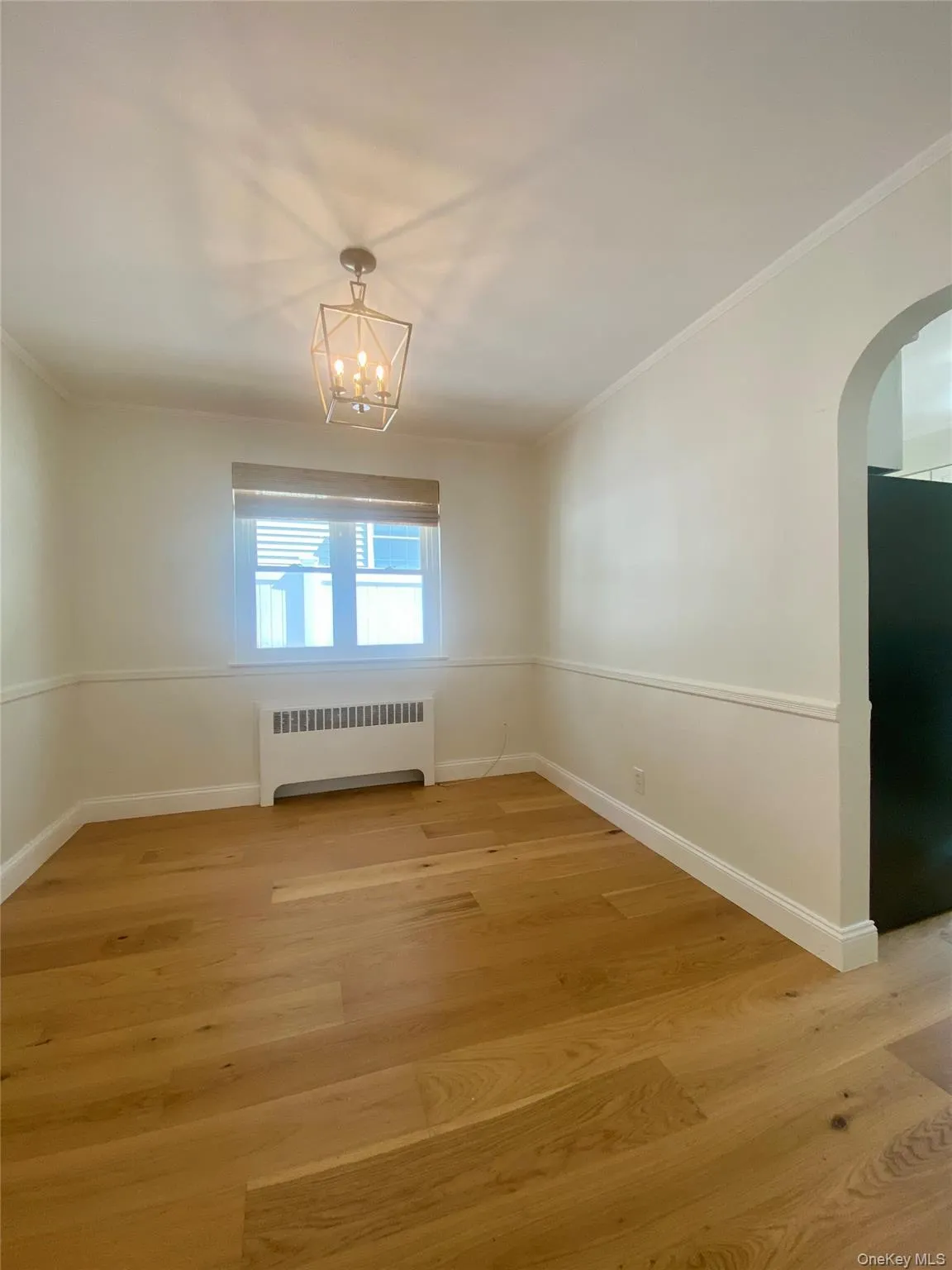 Empty room with light wood finished floors, radiator, arched walkways, and crown molding Empty room with light wood finished floors, radiator, arched walkways, and crown molding