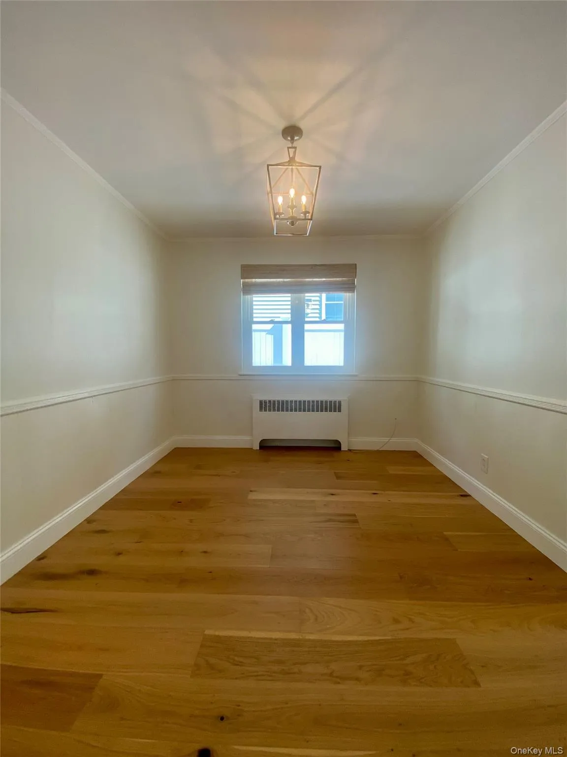 Unfurnished room with radiator heating unit, light wood-type flooring, crown molding, and a chandelier Unfurnished room with radiator heating unit, light wood-type flooring, crown molding, and a chandelier