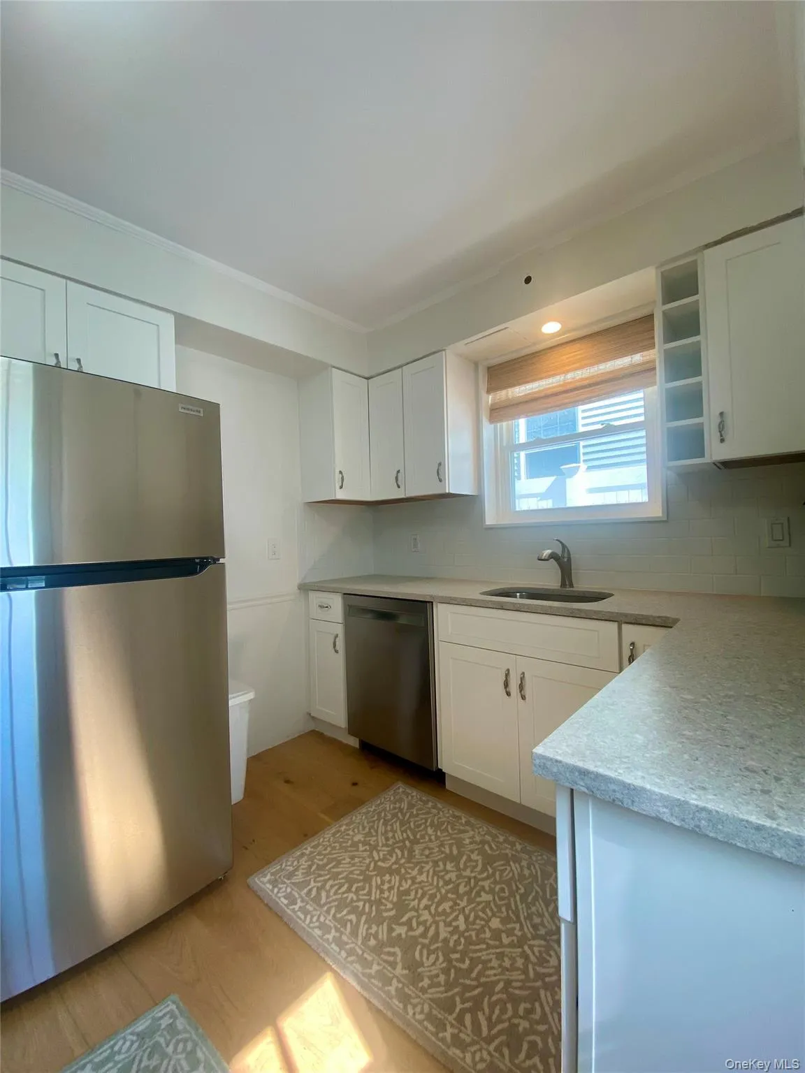 Kitchen with appliances with stainless steel finishes, white cabinets, open shelves, light wood finished floors, and light stone countertops Kitchen with appliances with stainless steel finishes, white cabinets, open shelves, light wood finished floors, and light stone countertops