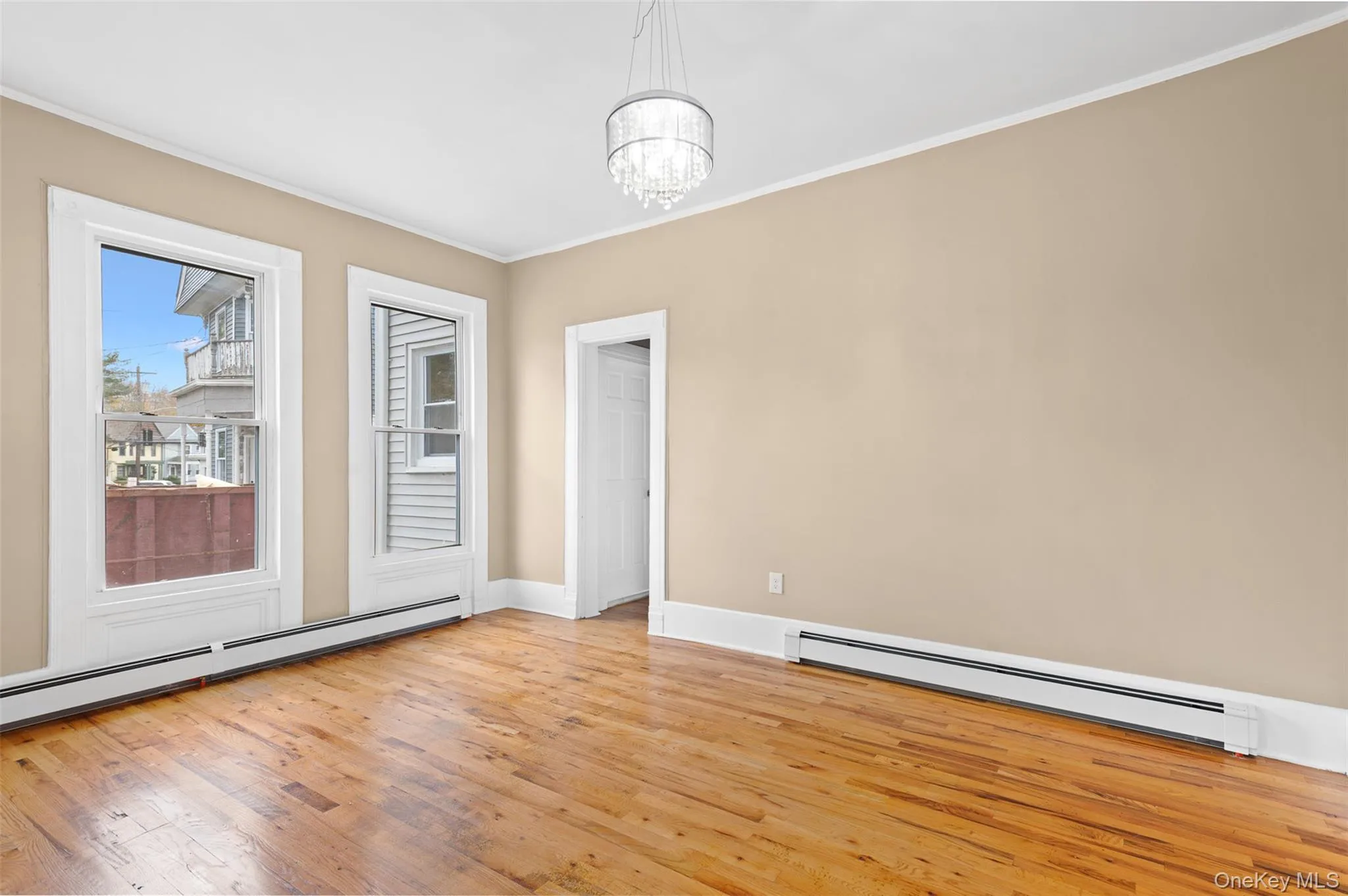Spare room featuring light wood-type flooring, ornamental molding, a baseboard radiator, and a chandelier Spare room featuring light wood-type flooring, ornamental molding, a baseboard radiator, and a chandelier