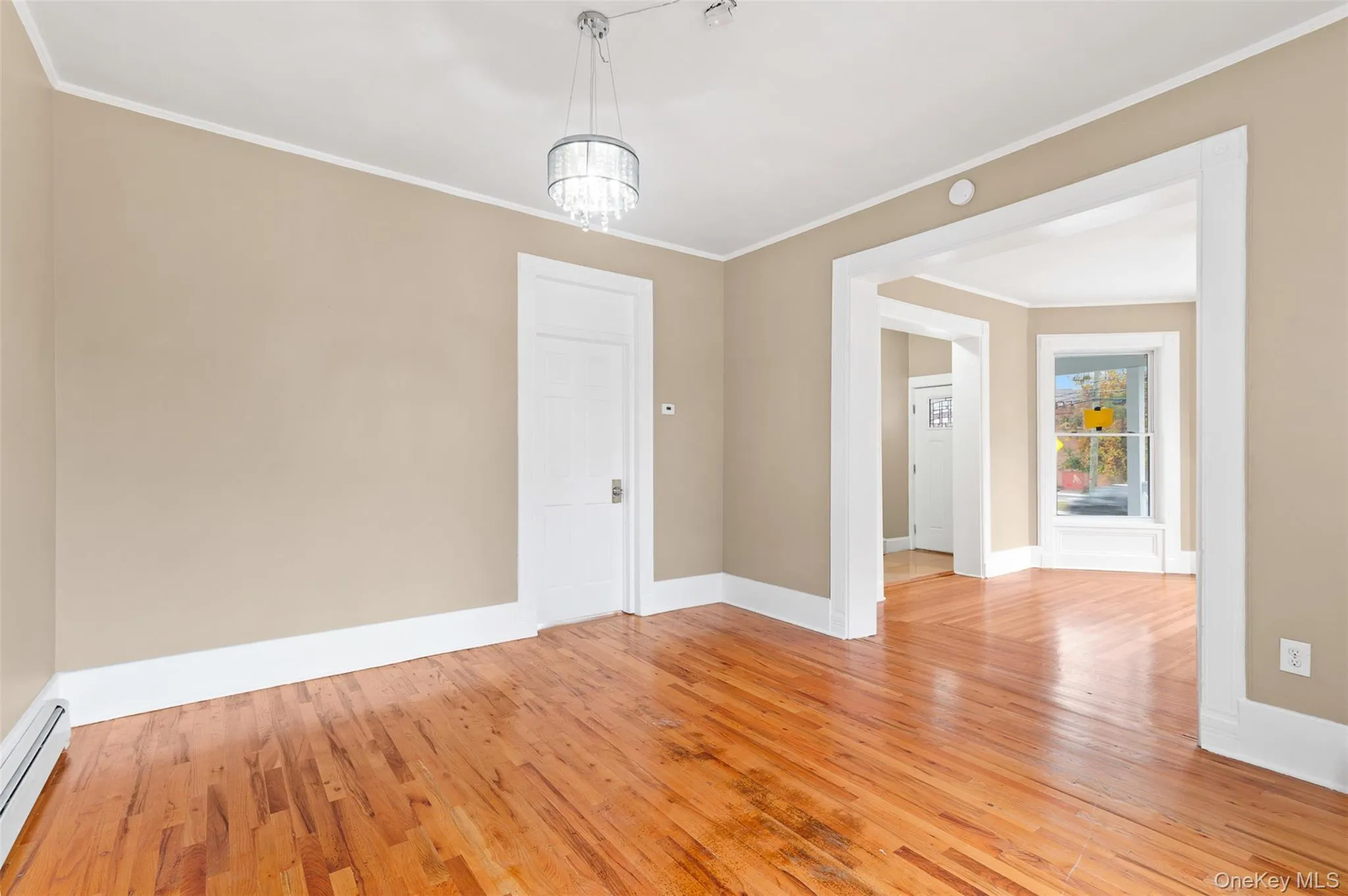 Unfurnished room featuring light wood-type flooring, ornamental molding, a baseboard radiator, and a chandelier Unfurnished room featuring light wood-type flooring, ornamental molding, a baseboard radiator, and a chandelier